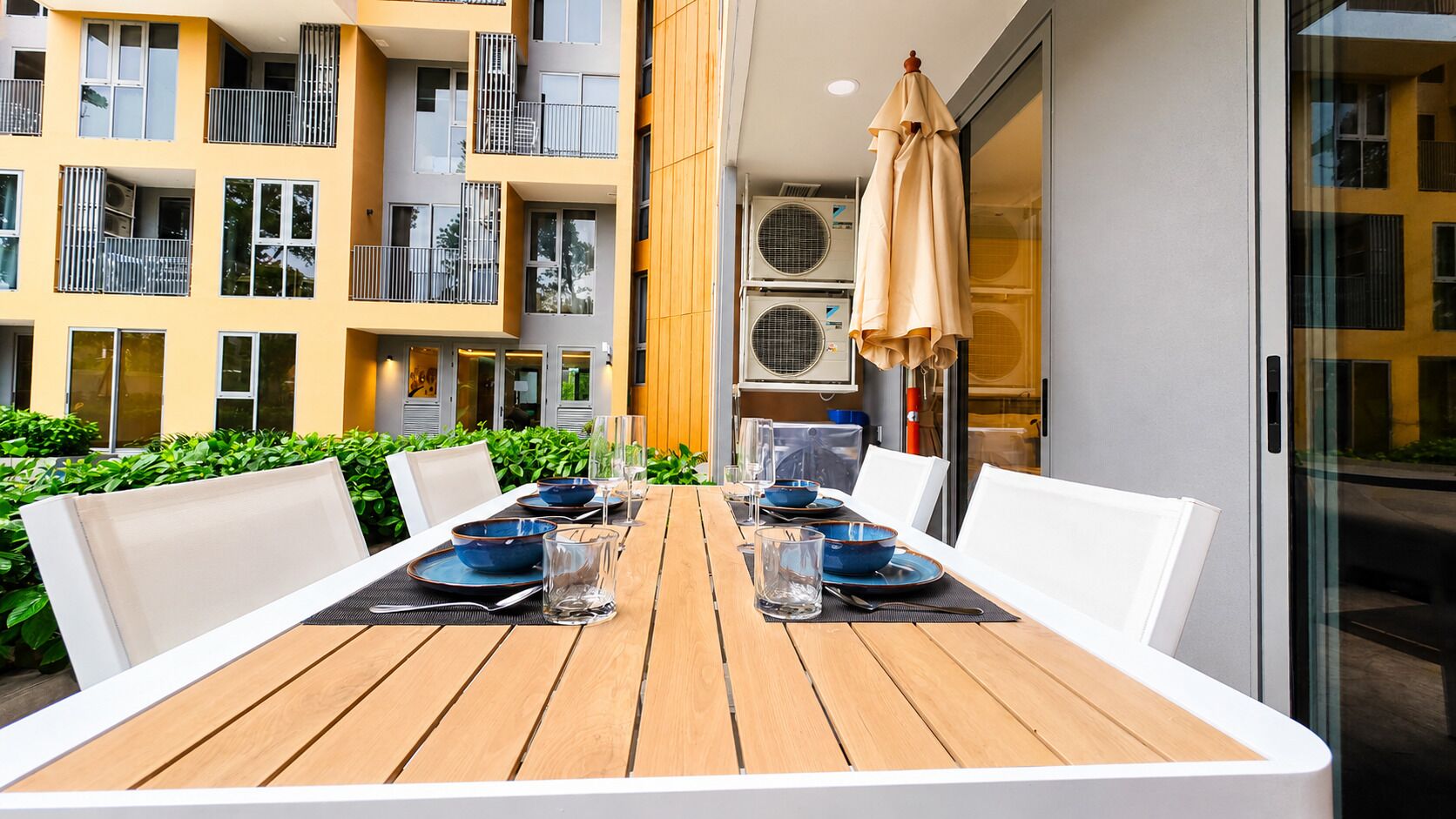 An outdoor dining area with a wooden table, white chairs, and blue bowls.