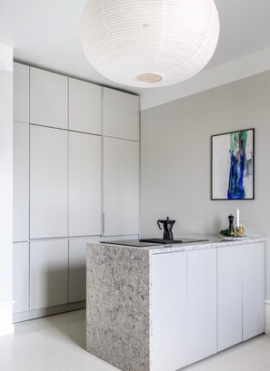 A modern kitchen with a marble island, white cabinetry, and a pendant light. - Luxury Apartment in a Prime Location with Netflix (Helsinki)