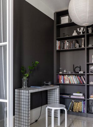 Moderni huone, jossa on tumma seinä, laatoitettu konsolipöytä, valkoinen jakkara ja kirjahylly, joka on täynnä kirjoja ja koriste-esineitä.