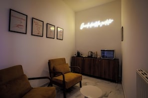 Ein Zimmer mit einem braunen Stuhl, einem kleinen runden Tisch, einer Holzküche mit Geräten und gerahmten Bildern an der Wand.
