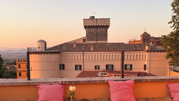 Una terrazza con tavolo e sedie, un vaso con fiori e vista su un edificio storico con una torre.