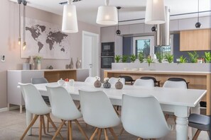 Eine moderne Küche mit Essbereich, ausgestattet mit einem weißen Tisch, Stühlen und Pendelleuchten.