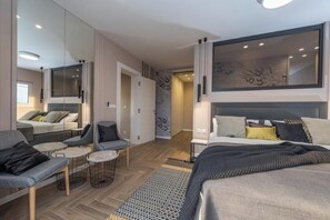 Ein modernes Hotelzimmer mit einem großen Bett, einer Sitzecke mit kleinem Tisch, einem Spiegel und Blick auf den Flur.