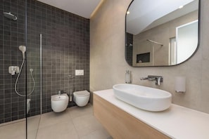 A modern bathroom with a large mirror, a white sink, a bidet, and a shower.