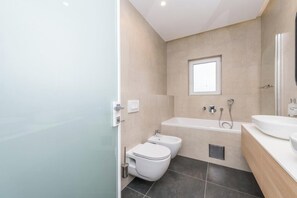 Een moderne badkamer met toilet, bidet, badkuip en een raam.