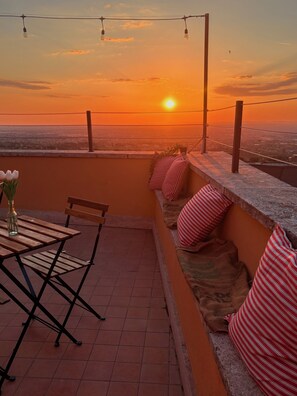 A terrace with a view of the sunset, a table with chairs, and a potted plant. - Vrbo Property (Frascati)