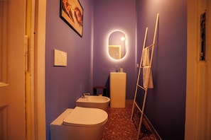 A bathroom with a toilet, bidet, sink, and a mirror with a light. - Vrbo Property (Frascati)