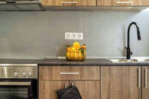 Een keuken met houten kastjes, een roestvrijstalen afzuigkap, een inbouwoven, een spoelbak met een zwarte kraan en een schaal fruit op het aanrecht.