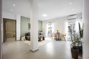 A modern living room with a sofa, coffee table, and a dining area with chairs and a table. - Spacious 1BR with Balcony l No Elevator (Athens)