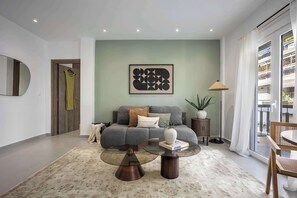 A modern living room with a grey sofa, a glass coffee table, and a large window with a view. - Spacious 1BR with Balcony l No Elevator (Athens)