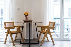 Een kamer met een ronde tafel, twee houten stoelen, een vaas met zonnebloemen en uitzicht door een glazen deur.