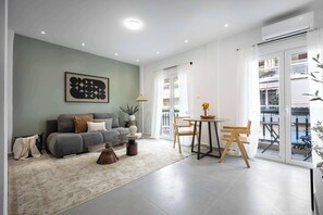 A modern living room with a sofa, coffee table, and chairs, a dining area with a table and chairs, and a large window with a view of a balcony. - Spacious 1BR with Balcony l No Elevator (Athens)