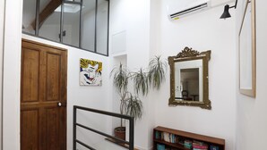 Een trap met een houten deur, een potplant, een boekenplank, een spiegel en een airconditioning.
