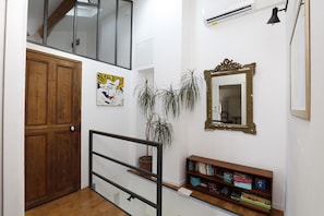 A staircase with a wooden door, a potted plant, a bookshelf, a mirror, and an air conditioning unit. - Les Airis, ecological vacation rental (Avignon)