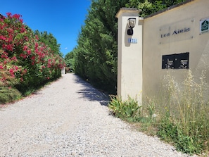 A gravel path leading to a building with a sign reading 'Les Airis' and a bike parking sign. - Les Airis, ecological vacation rental (Avignon)
