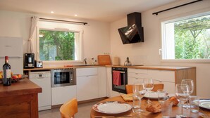 Een moderne keuken met een eethoek, voorzien van een vaatwasser, oven en een groot raam met uitzicht op bomen.