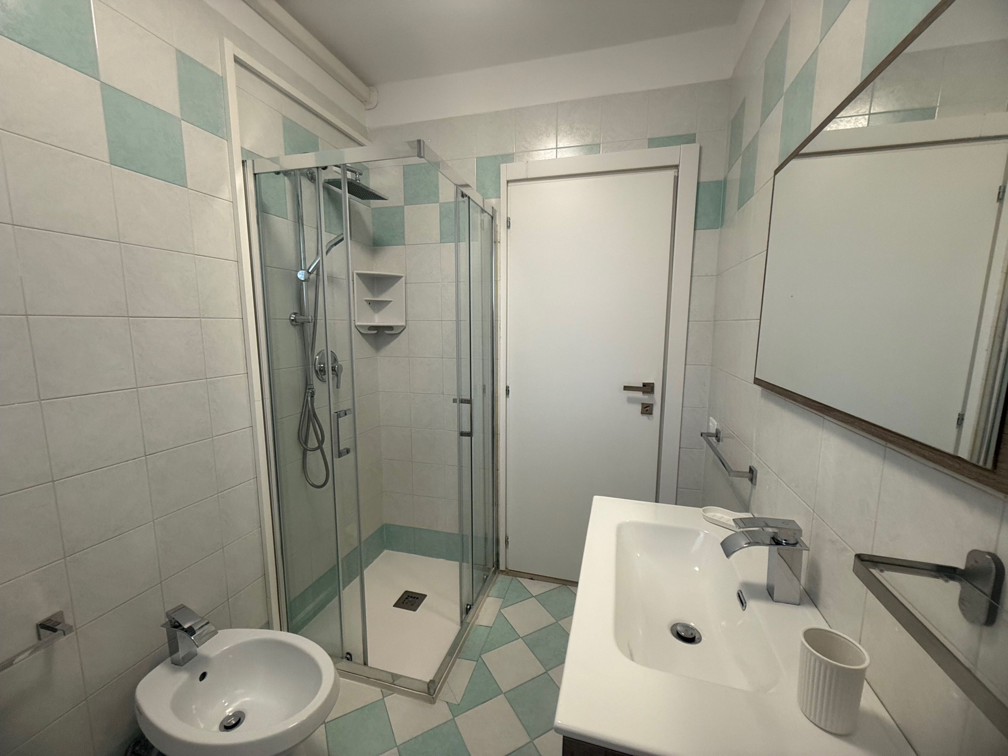 A bathroom with a glass-enclosed shower, a sink, and a mirror.