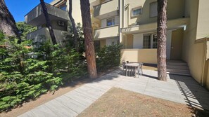 A courtyard with a wooden deck, a table and chairs, and a building with multiple balconies. - Spacious Apartment Near the Beach in Rosolina (Rosolina)