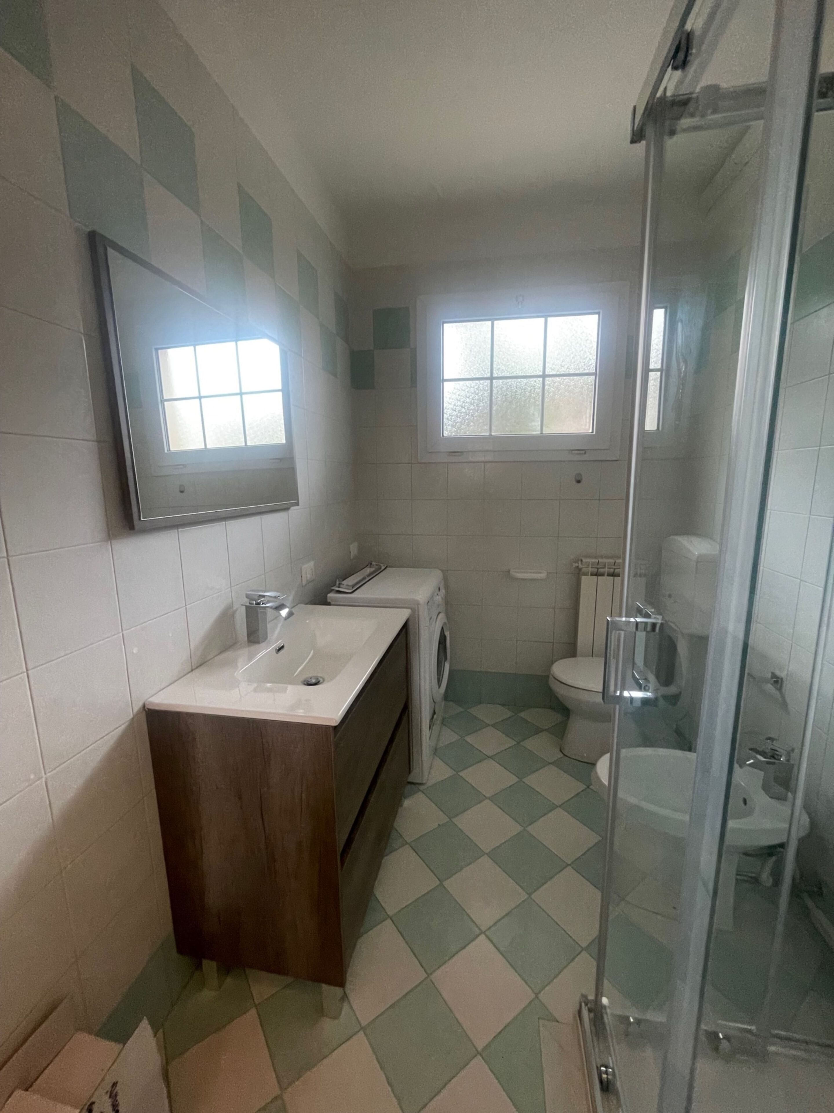 Et badeværelse med vask, spejl, vindue, toilet og brusebad.