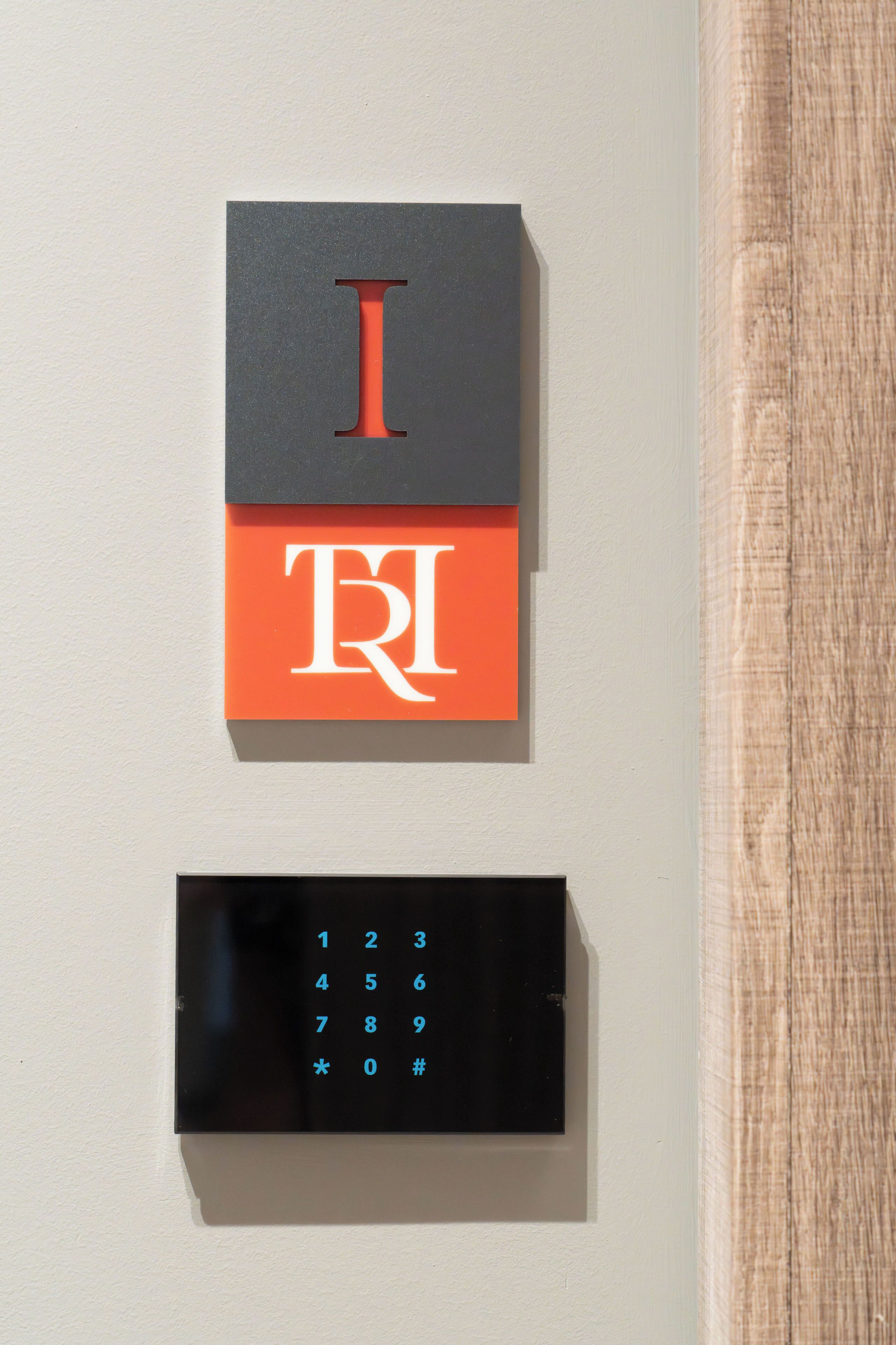 A wall-mounted electronic keypad with a numeric keypad and a red 'I' button.
