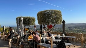 An outdoor seating area with tables and chairs, a sign for Andreas, and a view of the landscape. - Vrbo Property (Saint-Paul-de-Vence)