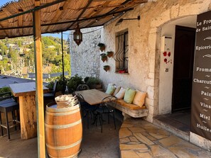 A rustic outdoor seating area with a wooden table, chairs, a barrel, and a stone floor. - Vrbo Property (Saint-Paul-de-Vence)