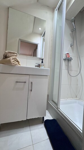 A bathroom with a glass shower enclosure, a white sink with a mirror, and a towel on the counter. - Vrbo Property (Saint-Paul-de-Vence)
