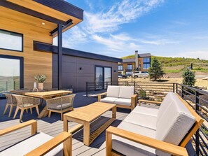 A modern outdoor patio with wooden furniture, a dining table, and a view of a hillside. - Modern Mountain Villa Near Deer Valley, Sleeps 14 (Heber City)