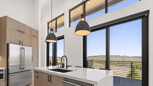 Una cocina moderna con un refrigerador de acero inoxidable, un lavavajillas y un amplio ventanal con vistas al paisaje.