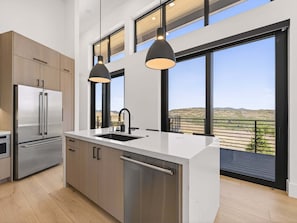 Una cocina moderna con un refrigerador de acero inoxidable, un lavavajillas y un amplio ventanal con vistas al paisaje.