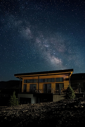 Un edificio moderno con amplios ventanales, un balcón y vistas al cielo nocturno.