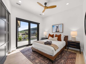A bedroom with a large bed, a ceiling fan, a view through a sliding door, and a painting on the wall. - Modern Mountain Villa Near Deer Valley, Sleeps 14 (Heber City)