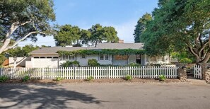A two-story house with a white picket fence, a garage, and a garden with small plants. - Oak & Ivy Cottage - Heart of Montecito (Santa Barbara)