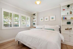 Une chambre à coucher avec un grand lit, une table de chevet, une bibliothèque et une fenêtre avec des stores.