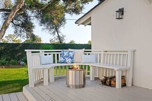 A white outdoor seating area with a fire pit, a bench, and a white wall in the background. - Oak & Ivy Cottage - Heart of Montecito (Santa Barbara)