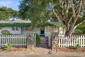 Une maison avec un portail en pierre, une clôture blanche en bois et un chemin menant à l’entrée.