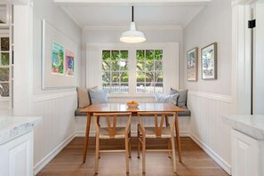 Un espace repas comprenant une table et des chaises en bois, un banc avec des coussins et un luminaire suspendu.