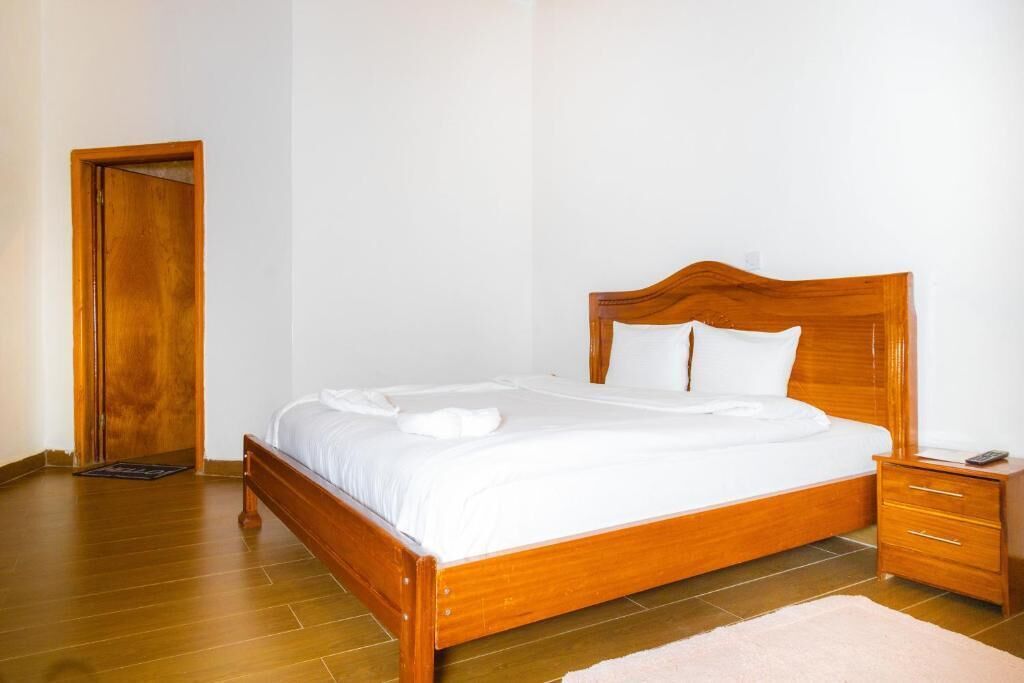 A neatly made bed with white linens, a wooden headboard, a bedside table with a drawer, and a wooden door.