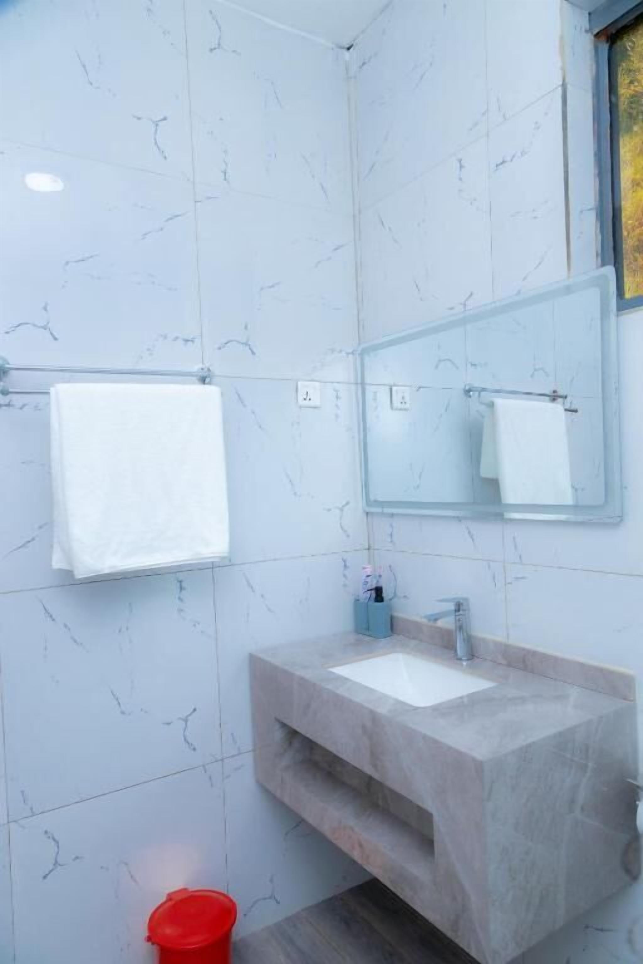 Une salle de bain avec un mur en marbre, un lavabo, un miroir et un seau rouge.