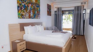 A modern bedroom with a large bed, a nightstand, a wooden headboard, and a colorful abstract painting on the wall. - Ruhondo Beach Resort (Gashaki)