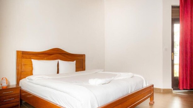 Una cama bien hecha en una habitación con cabecera de madera, una mesita de noche con lámpara y una cortina roja.