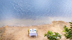 Una mesa de comedor con sillas sobre una playa arenosa, con vista a una masa de agua.
