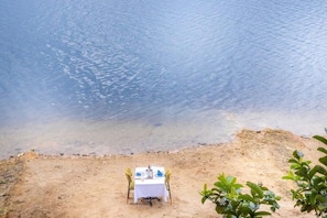A dining table with chairs on a sandy beach, overlooking a body of water.