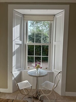 Ein Eckzimmer mit Erkerfenster, zwei weiße Stühle und ein Tisch mit Blumenvase.