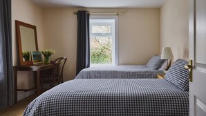 Een slaapkamer met twee bedden, een bureau met stoel, een spiegel en een raam met gordijnen.