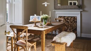 Een eetkamer met een houten tafel, stoelen, een hanglamp, een open haard en een spiegel aan de muur.