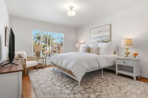 A bedroom with a bed, bedside tables, a chair, a TV, and a window with a view. - The Palm Terrace - West Beach Retreat (Santa Barbara)