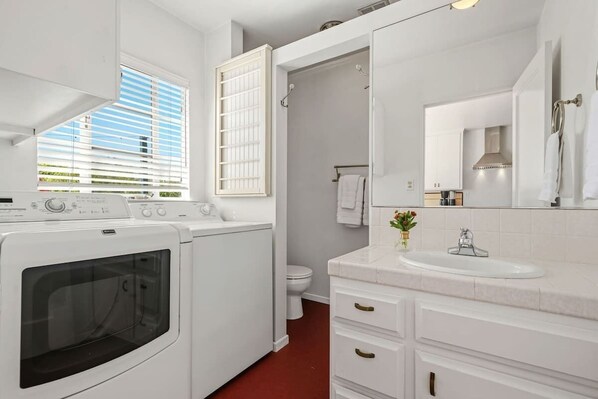 A modern bathroom with a built-in washing machine, a large mirror, and a white sink. - The Palm Terrace - West Beach Retreat (Santa Barbara)