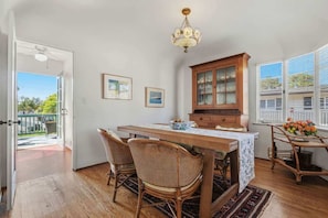 A dining area with a wooden table, wicker chairs, a cabinet, and a chandelier. - The Palm Terrace - West Beach Retreat (Santa Barbara)
