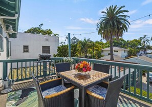 A balcony with wicker furniture, a wooden table, and a vase of flowers. - The Palm Terrace - West Beach Retreat (Santa Barbara)